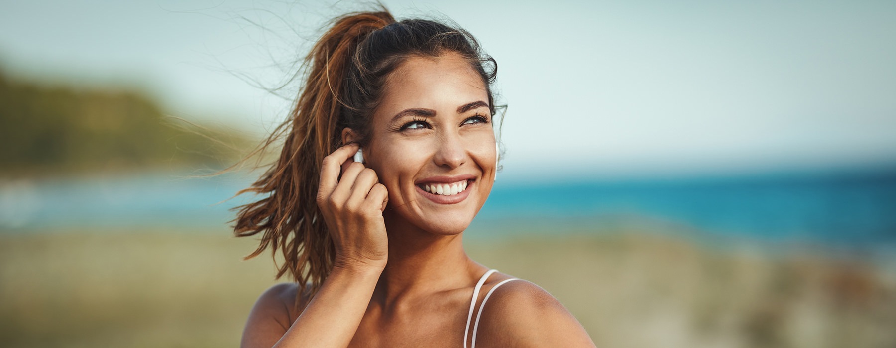 young woman with a ponytail puts in her earbud before exercising near the water