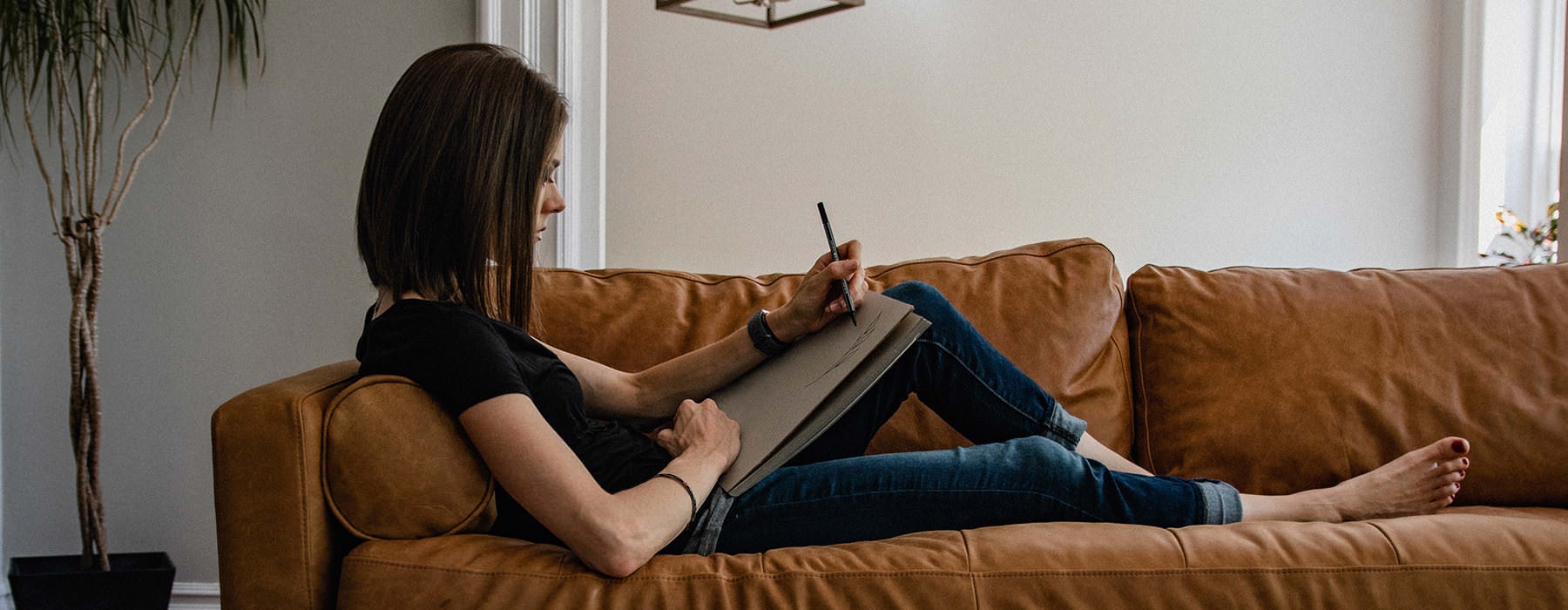 woman reclines on her sofa and sketches on a drawing pad