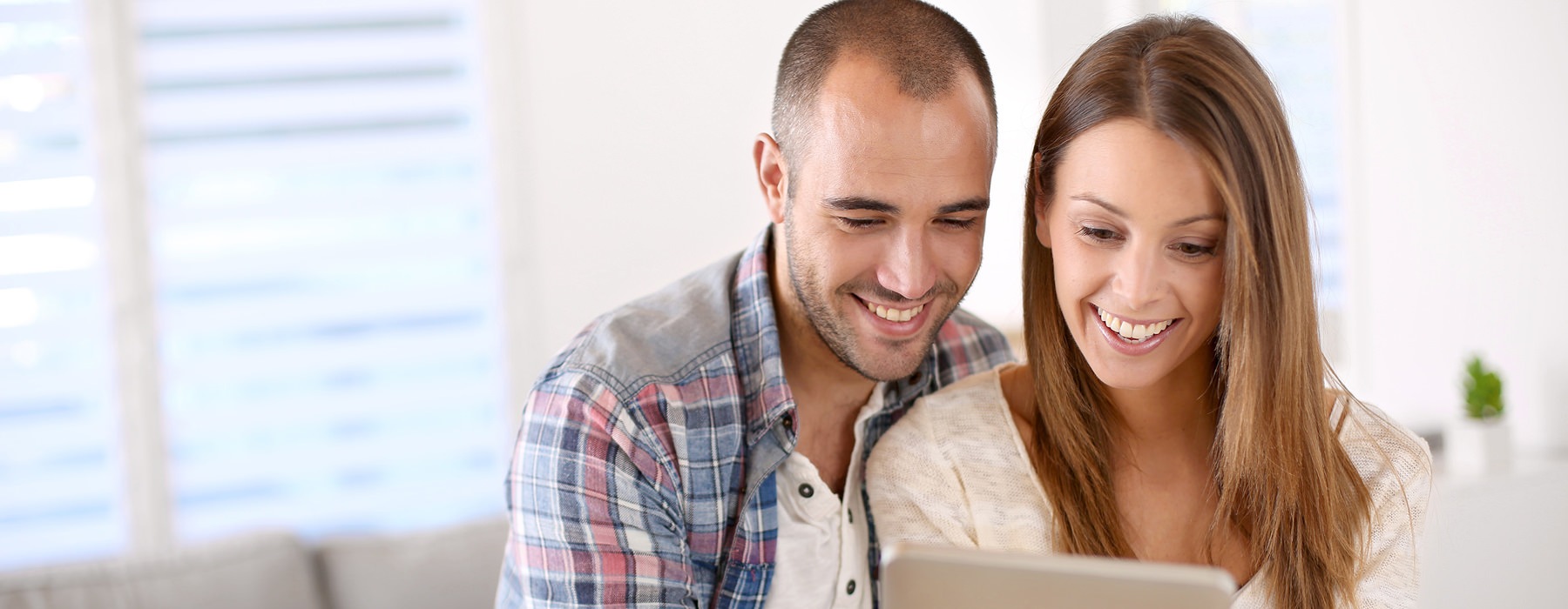 young couple sit in their living room and look at an ipad